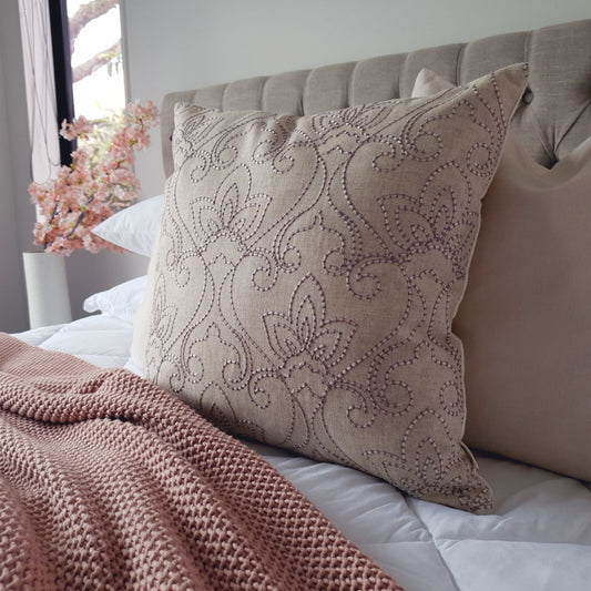 Decorative Threads Indie cushion with floral pattern on a bed with pink blanket and flowers in the background