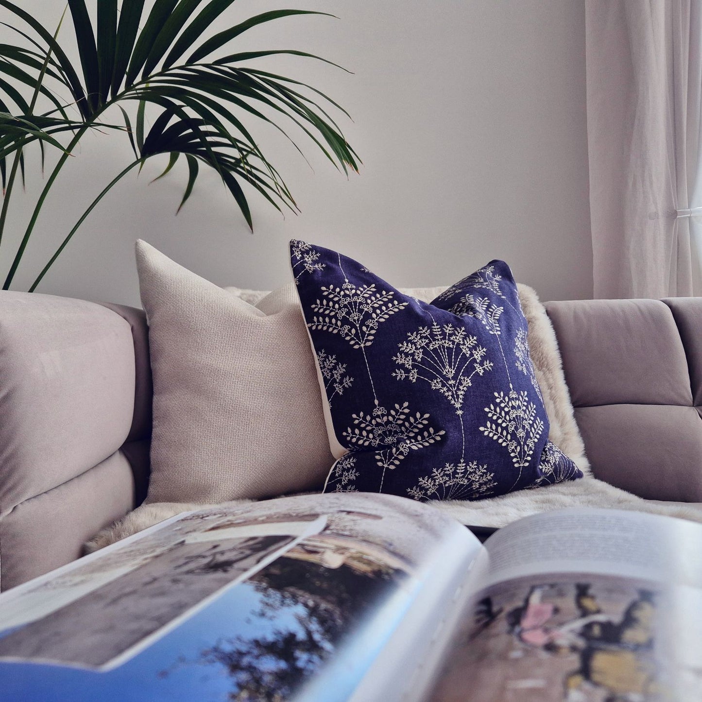 Decorative Threads Regal indigo cushion on a sofa with an open magazine and plant in the corner.