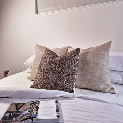 Decorative Threads Herringbone Harmony cushion combo in colour natural/mocha on a bed with Bed with open magazine on a light-colored background.