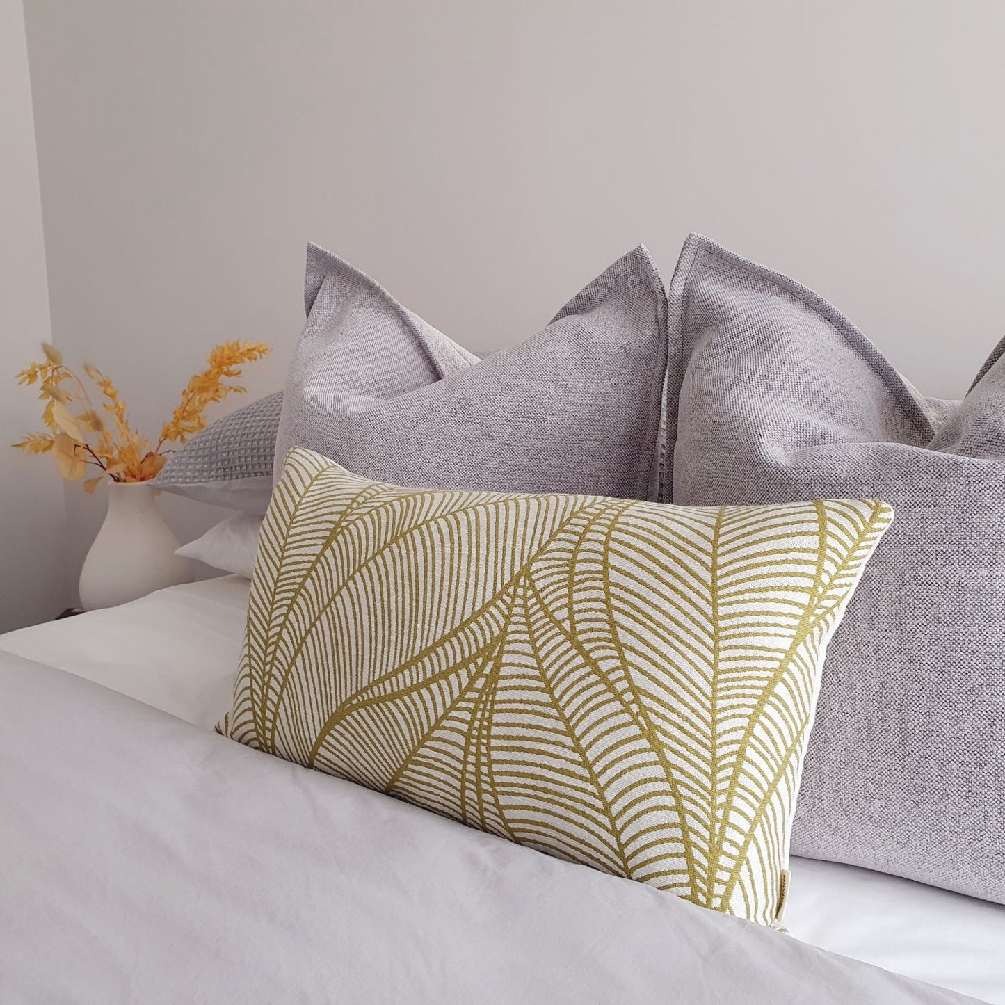 Decorative Threads Hutt cushion in grey on a bed with a vase of flowers in the background.
