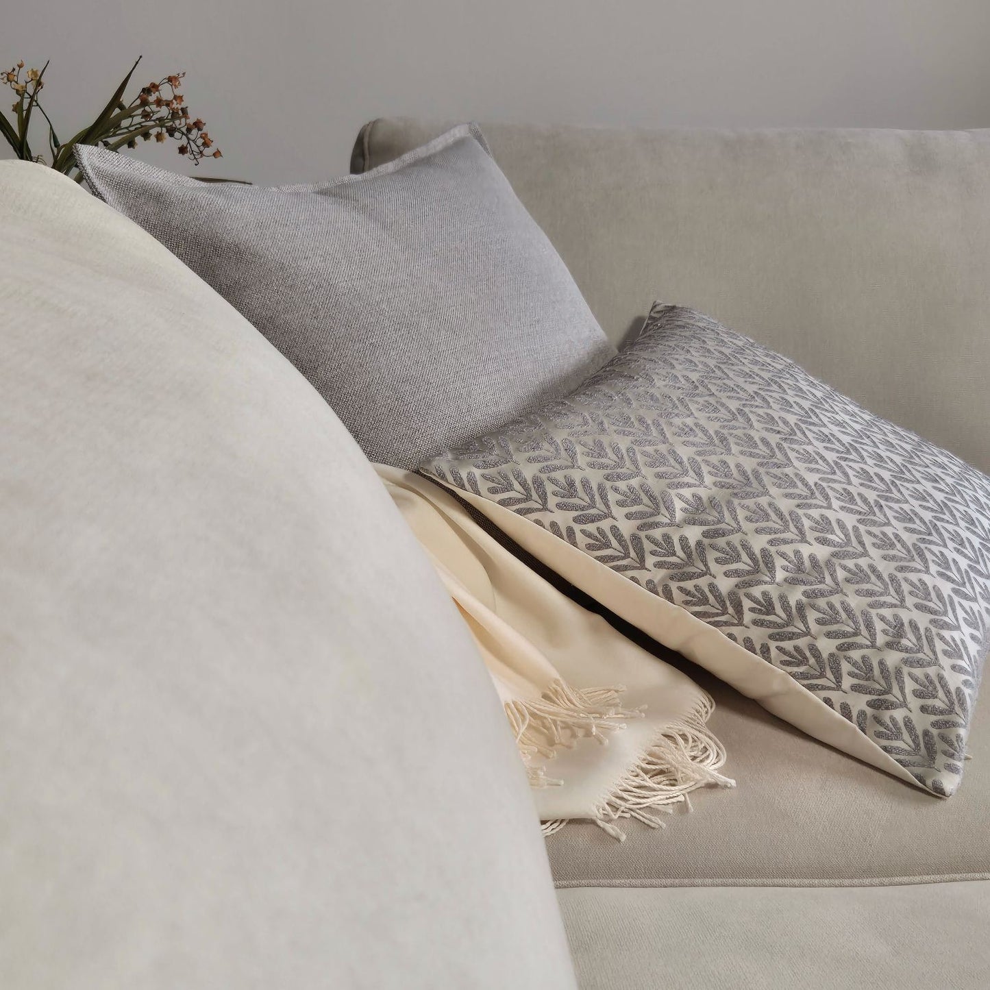Decorative Threads Willow siliver and Hutt grey cushion covers with throw blanket on a beige sofa with a neutral background