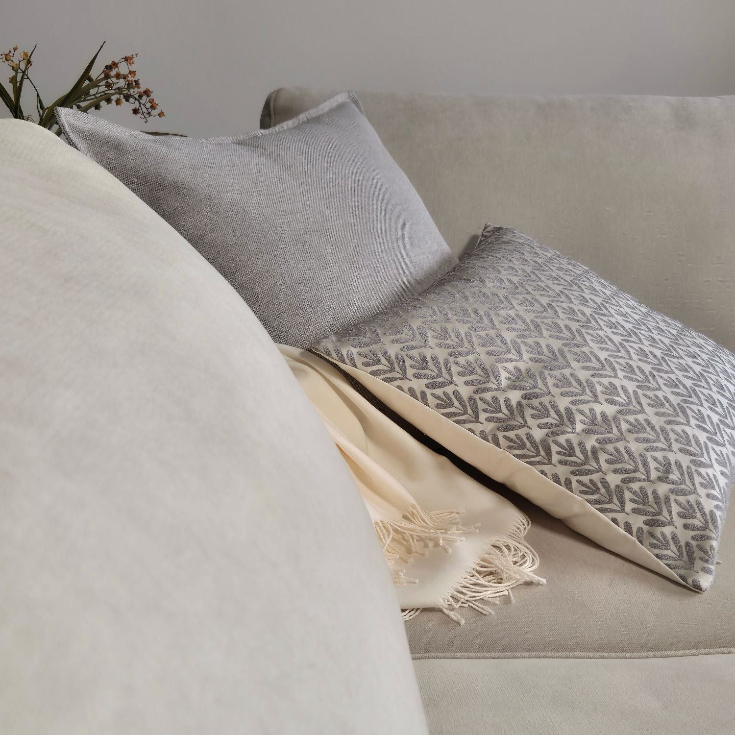 Decorative Threads Willow siliver and Hutt grey cushion covers with throw blanket on a beige sofa with a neutral background