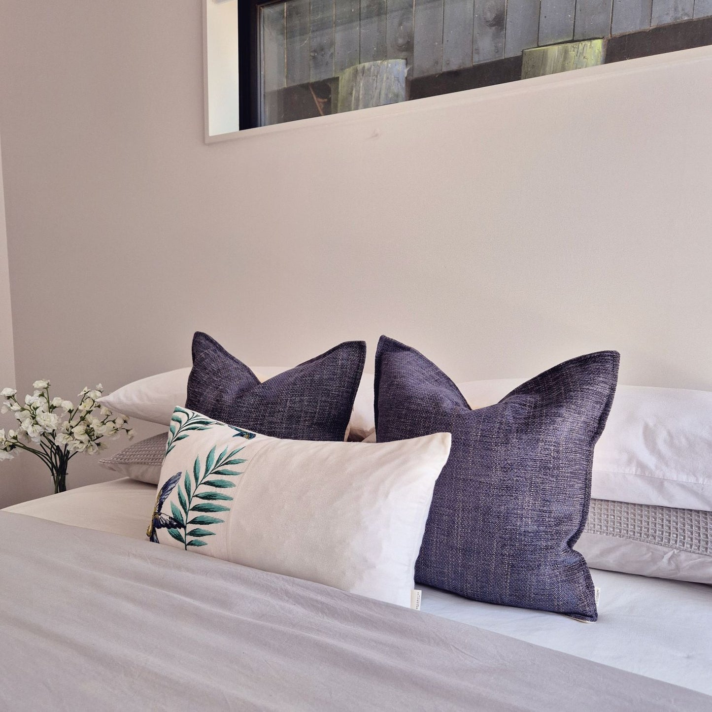 Avian Ivory embroidered botanical bird cushion paired with Twilight dark blue covers for a sophisticated, dreamy bedroom look by Decorative Threads.