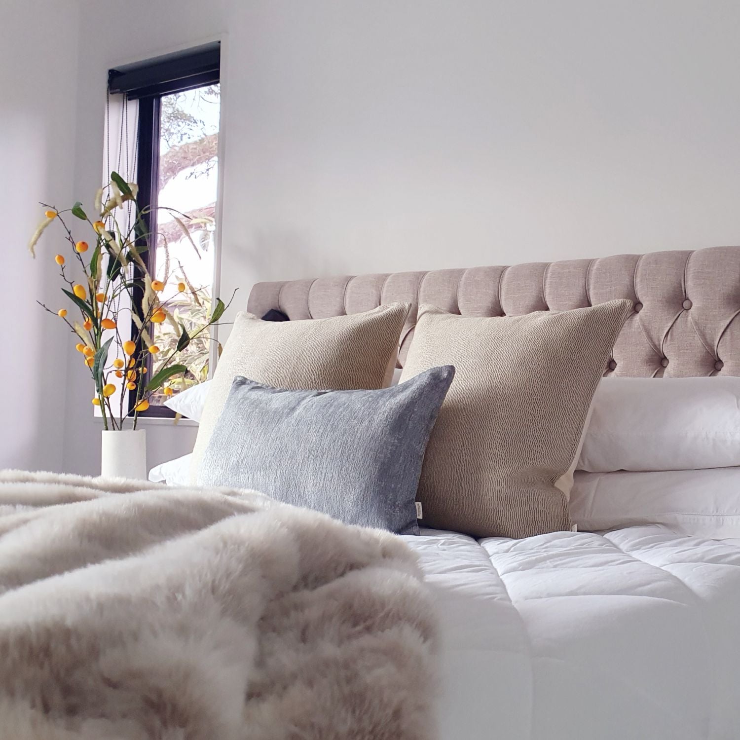 Decorative Threads katama cushions on a neatly made bed with a vase of flowers in a bedroom