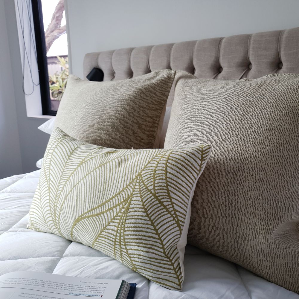 Decorative Threads Katama cushions in colour brulee with vein cushion with leaf pattern on a bed with a tufted headboard.