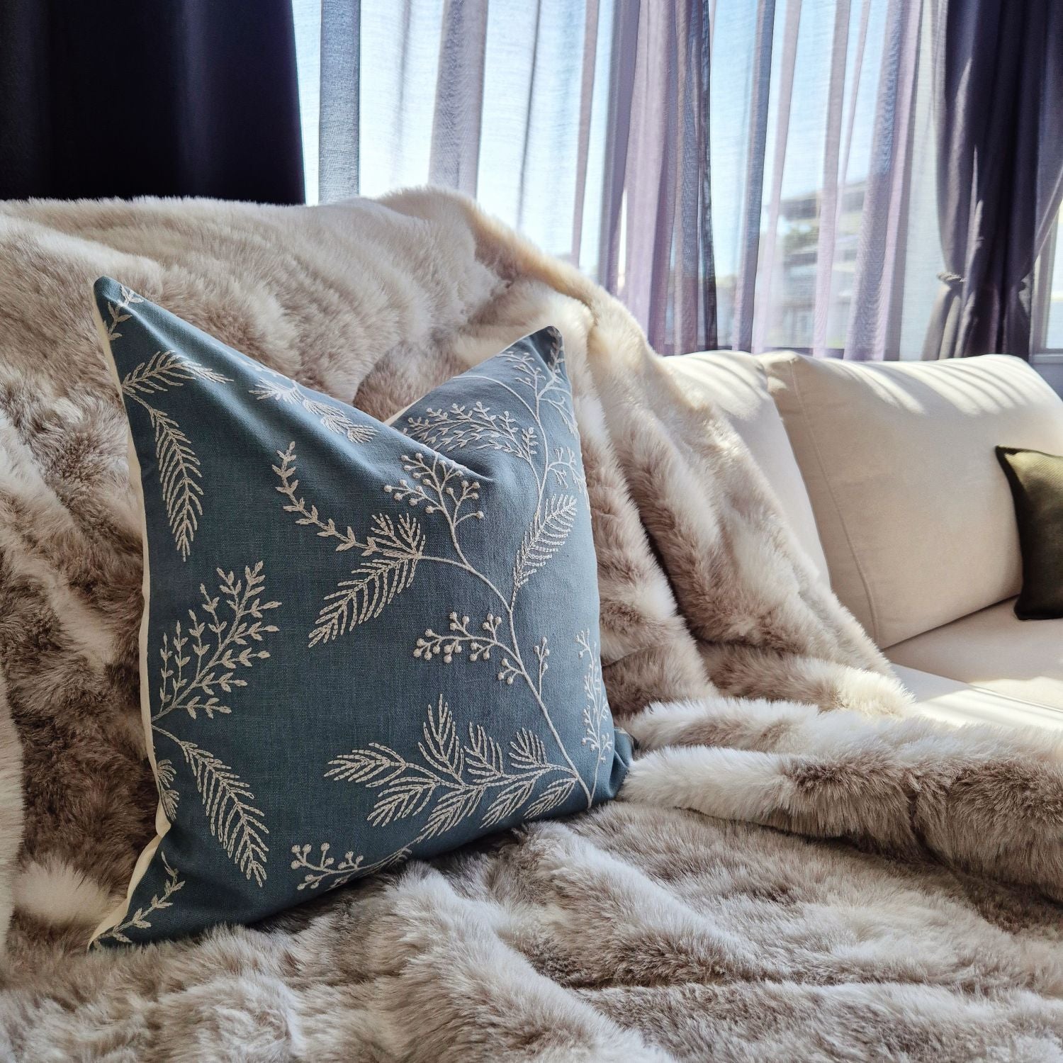 Decorative threads medley cushion with leaf pattern on a fluffy blanket in a cozy living room.