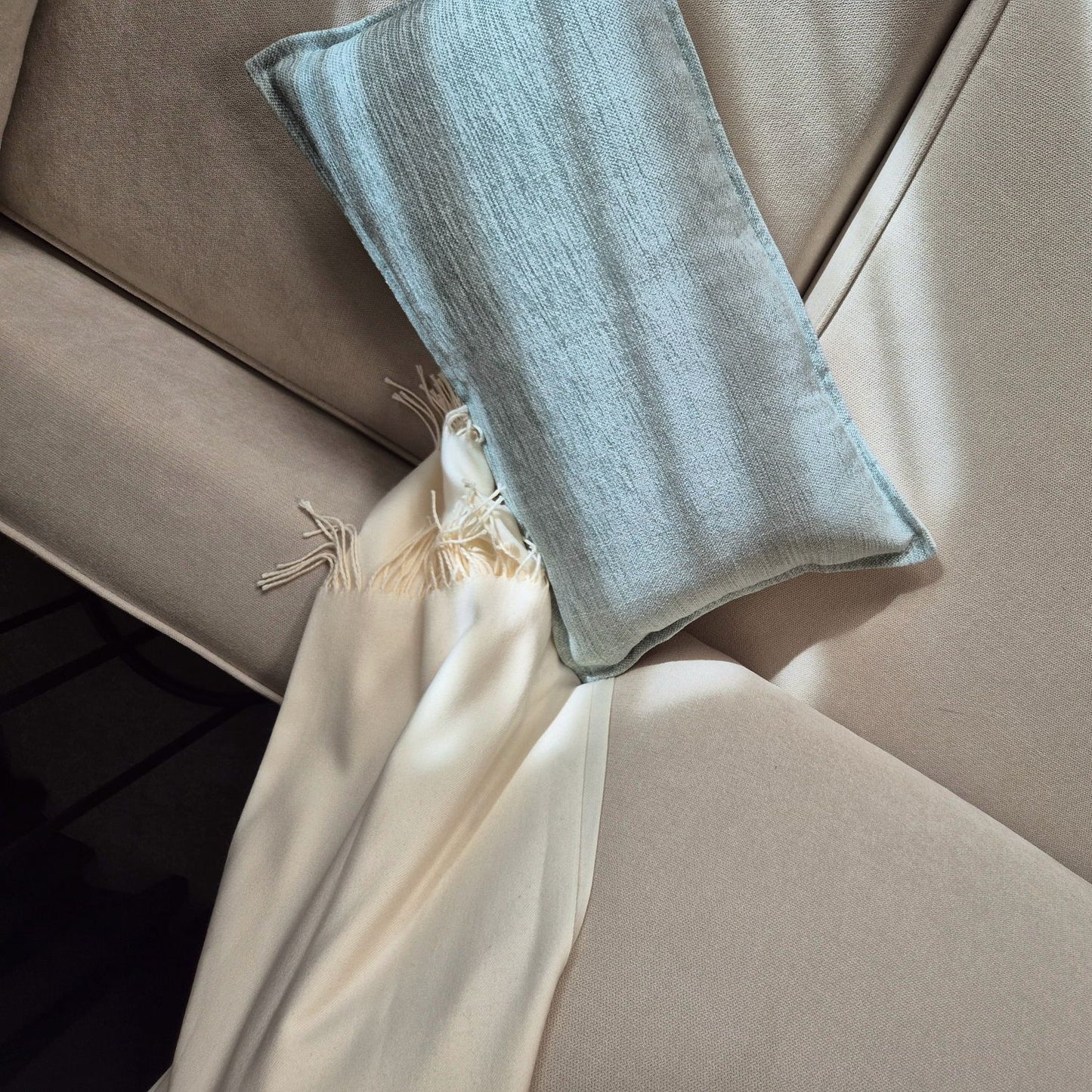 Decorative Threads Misty cushion in duckegg blue with a throw with fringes on a beige sofa.