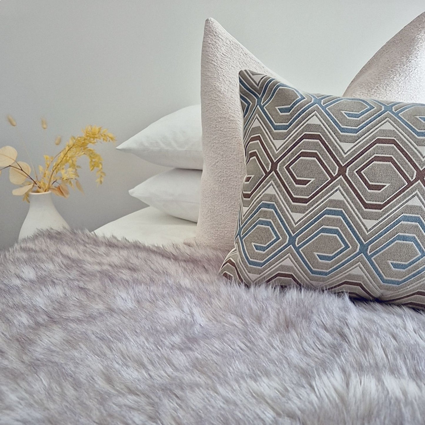 Decorative Threads cushion combo with a Chunky Tweed cover paired with a geometric pattern placed on a bed with a fur blanket in a neutral background. 
