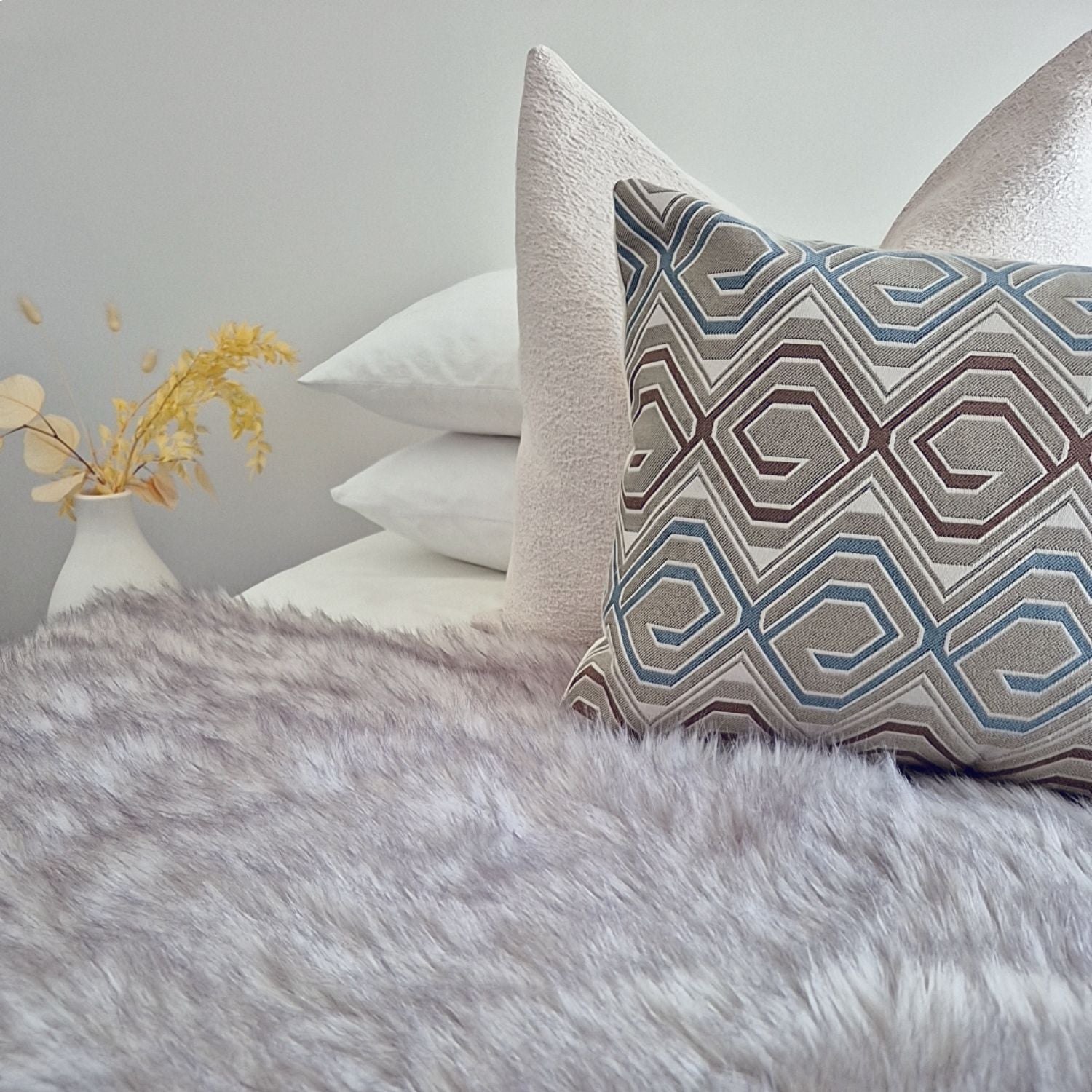 Decorative Threads cushion combo with a Chunky Tweed cover paired with a geometric pattern placed on a bed with a fur blanket in a neutral background. 