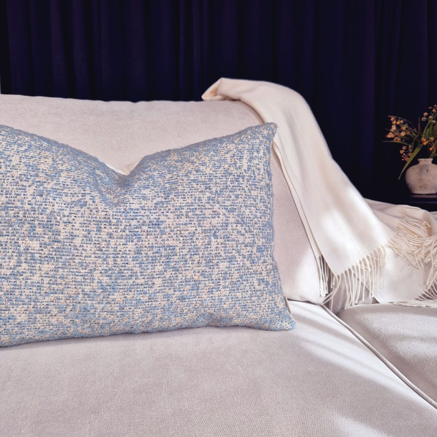 Decorative Threads light blue Textured  cushion on a cream sofa with a white blanket and dark background