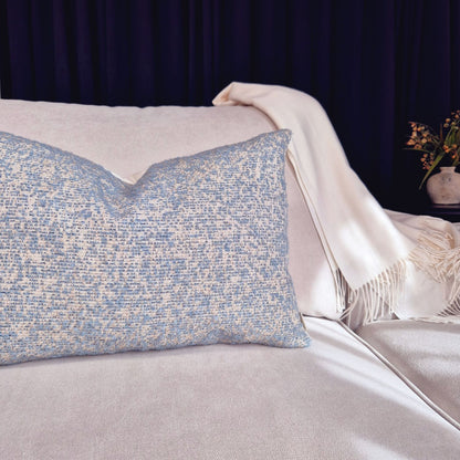 Decorative Threads light blue Textured  cushion on a cream sofa with a white blanket and dark background