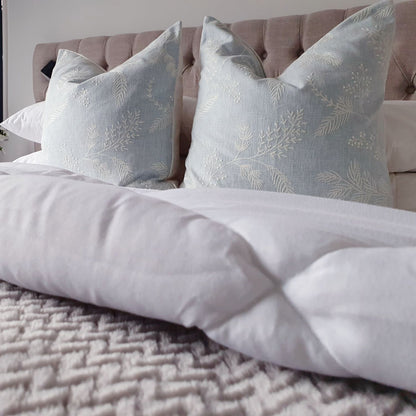 Decorative Threads Spruce embroidered cushions on  a bed with white bedding 