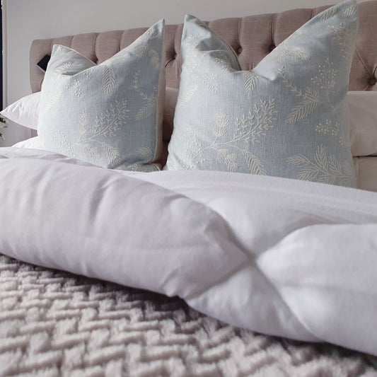 Decorative Threads Spruce embroidered cushions on  a bed with white bedding 