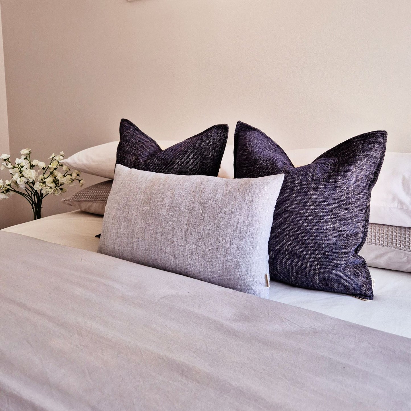 Neatly arranged cushions on a bed with a neutral background