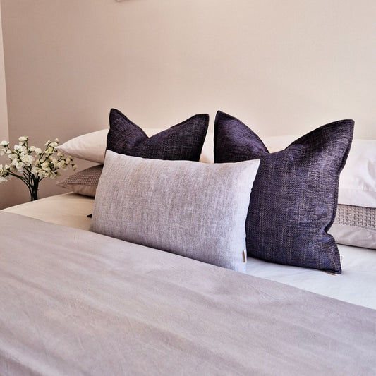 Neatly arranged cushions on a bed with a neutral background